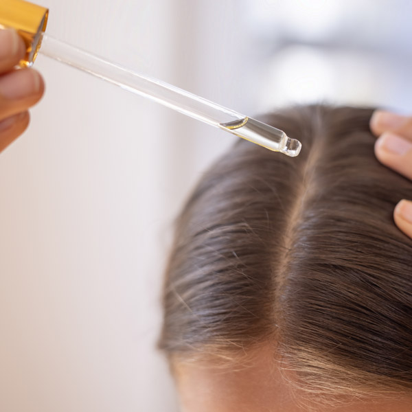 close up of woman putting oil in her hair with dropper